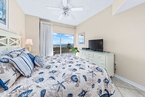Een slaapkamer met een bed, een televisie, een plafondventilator, een balkon met uitzicht en een plant.