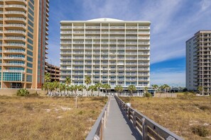 A multi-story hotel with a central atrium, surrounded by a boardwalk and palm trees. - Tidewater 208 | Pools, Gym, Hot Tub, Wifi | Private Balcony | Ocean Front Views (Orange Beach)