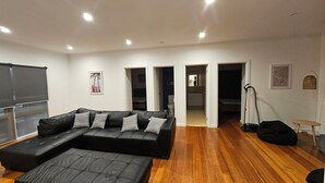 Uma sala de estar moderna com um sofá seccional, piso de madeira e teto com iluminação embutida.