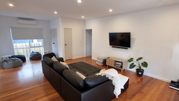 Uma sala de estar moderna com um sofá modular preto, uma TV de tela plana, uma planta em vaso e um abajur.