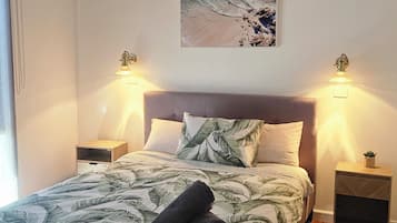 A bedroom with a bed, a ceiling fan, two bedside lamps, a wall-mounted picture, and a wooden floor.