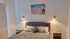 Quarto com cama, soalho de madeira, um quadro na parede e duas luminárias de cabeceira.