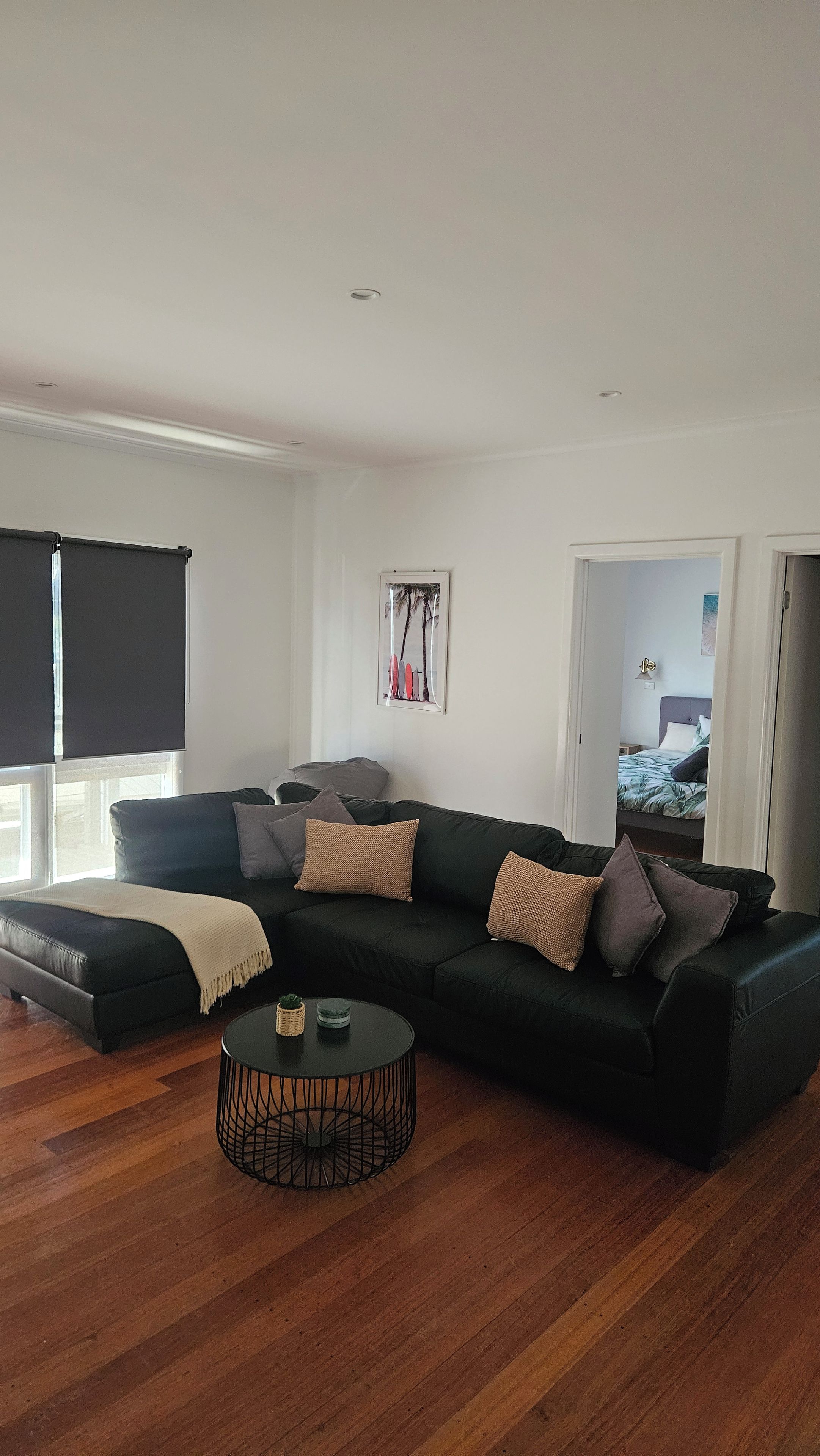 A modern living room with a sectional sofa, a round coffee table, and a large window with blinds.