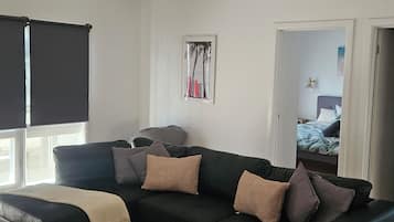 A modern living room with a sectional sofa, a round coffee table, and a large window with blinds.