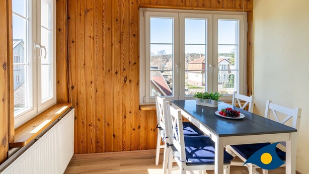 A dining area with a wooden wall, large windows, and a table with chairs. - Beach villa Whg 02 - SVB 02 (Heringsdorf)