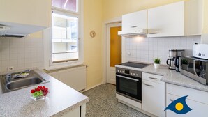 A kitchen with white cabinets, a stainless steel sink, a stove, and a microwave. - Beach villa Whg 02 - SVB 02 (Heringsdorf)