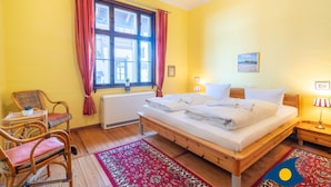 A room with a wooden bed, a window with red curtains, a small table with a chair, and a nightstand with a lamp. - Beach villa Whg 01 - SVB 01 (Heringsdorf)