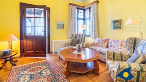 A room with a wooden floor, a sofa set, a table with a vase, a lamp, a chair, a door, and a window with curtains. - Beach villa Whg 01 - SVB 01 (Heringsdorf)