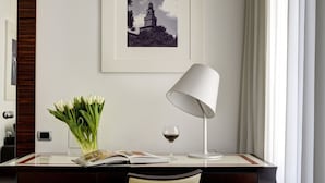 A desk with a lamp, a glass vase with flowers, a wine glass, and a framed picture on the wall. - Milano Castello Luxury Apartment (Milan)