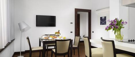 A dining area with a round table, chairs, a flat-screen TV, a vase with flowers, and a framed picture on the wall.