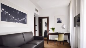 A modern hotel room with a black leather sofa, a desk with a chair, a TV, and framed pictures on the walls. - Milano Castello Luxury Apartment (Milan)