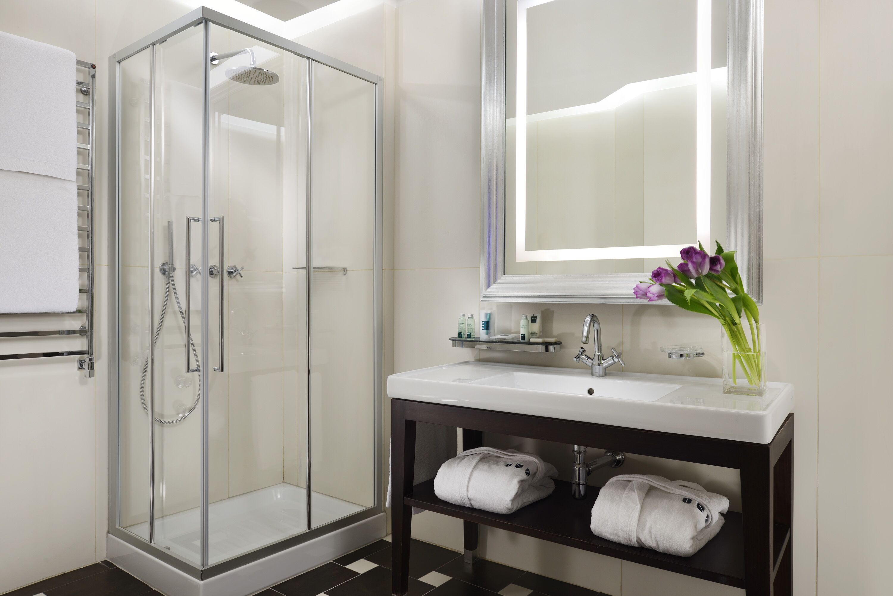 A modern bathroom with a glass-enclosed shower, a white sink with a mirror above, and a vase with flowers on the vanity.