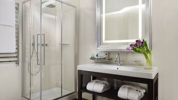 A modern bathroom with a glass-enclosed shower, a white sink with a mirror above, and a vase with flowers on the vanity.