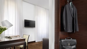 A hotel room with a wooden desk, a chair, a flat-screen TV, a bed, and a wardrobe with a suit and a briefcase. - Milano Castello Luxury Apartment (Milan)