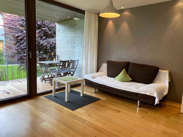 A modern living room with a sofa, a dining table with chairs, and a sliding glass door leading to an outdoor area.