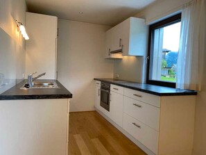 A compact kitchen with white cabinets, a black countertop, a window with a view, and a wooden floor.