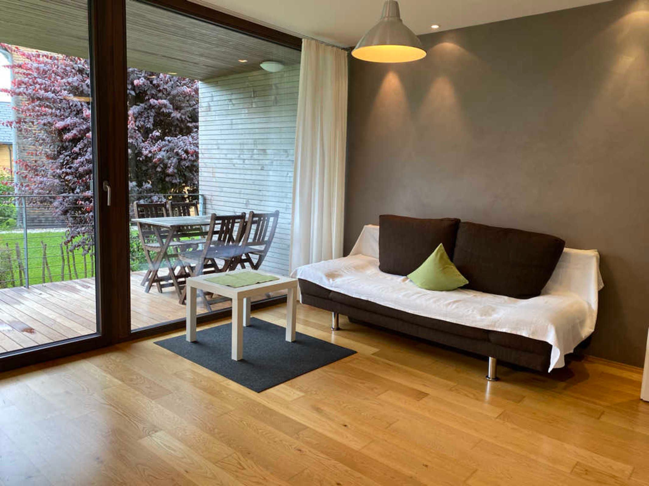 Ein modernes Wohnzimmer mit einer Couch, einem Esstisch mit Stühlen und einer Glastür, die zu einem Außenbereich führt.