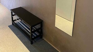 Huoneessa on metallinen hyllykkö, penkki ja suuri peili seinällä.