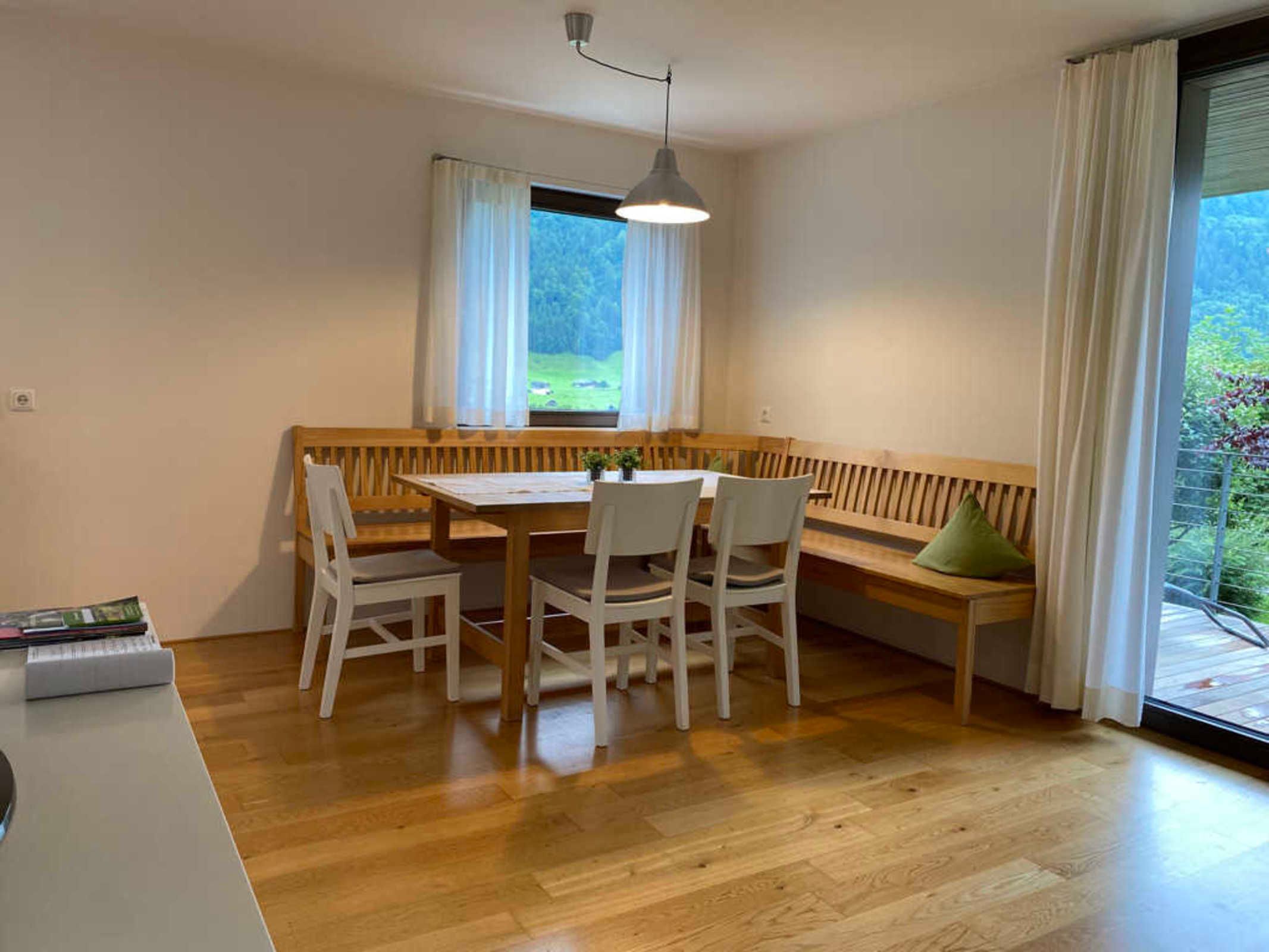 Une pièce avec un banc en bois, une table avec des chaises, une lampe suspendue et une fenêtre avec des rideaux.