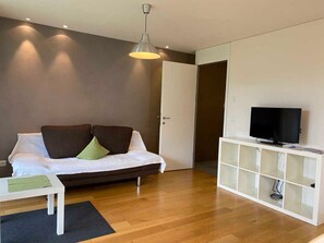 A modern room with a sofa, a television on a white cabinet, and a door leading to another room.