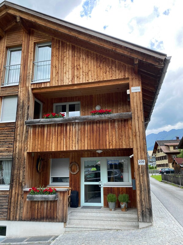 A wooden two-story building with a balcony, a sign indicating it is a guesthouse, and a number sign '230'.