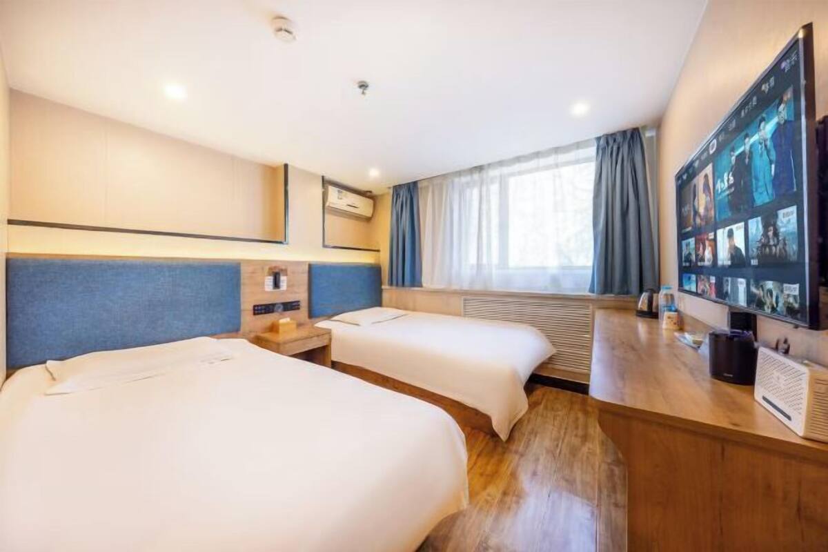 Habitación de hotel con dos camas, televisión, escritorio y ventana con cortinas.