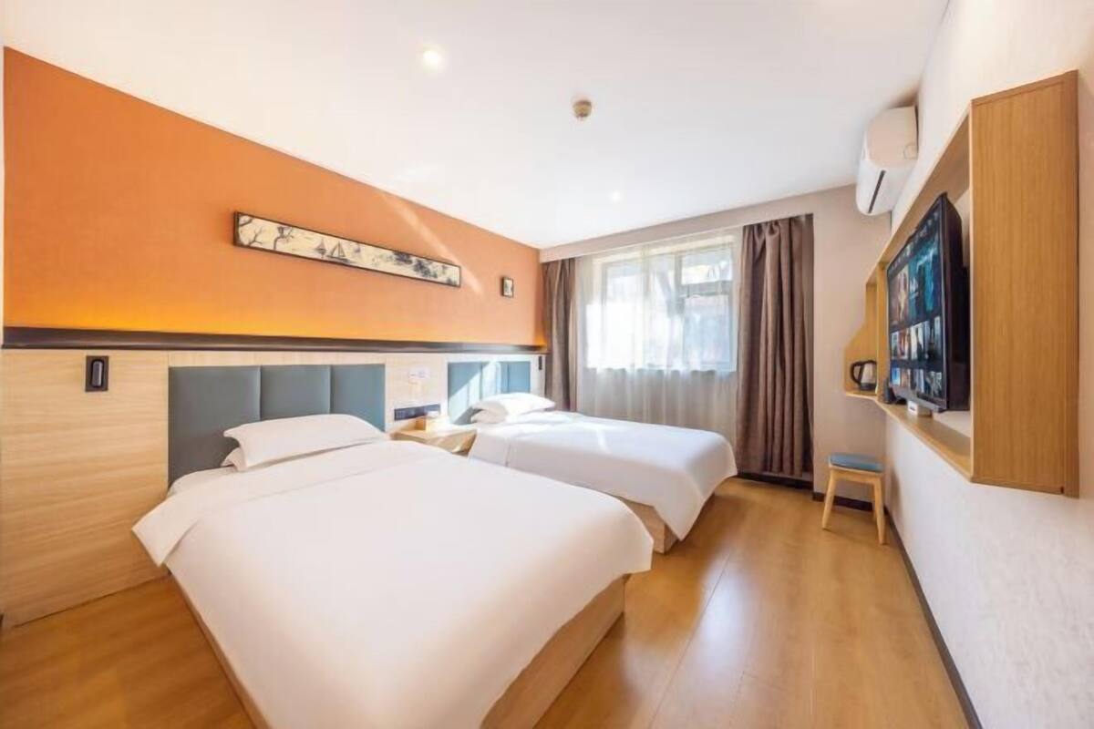 Habitación de hotel con dos camas, un televisor de pantalla plana, una mesita y una ventana con cortinas.