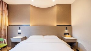 A hotel room with a large bed, two bedside tables, a green chair, and a wall-mounted light fixture. - Rest Hotel (Lanzhou West Railway Station Lanzhou Old Street) (Lanzhou)