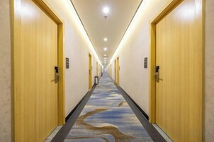 Un pasillo de hotel con puertas de madera, alfombra estampada e iluminación empotrada en el techo.