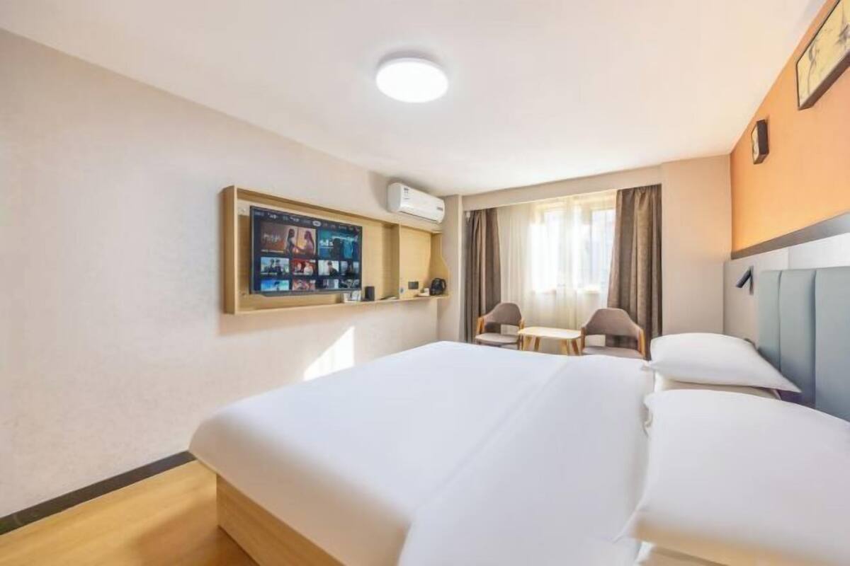 Habitación de hotel con una cama grande, un escritorio con silla, un televisor montado en la pared y una ventana con cortinas.