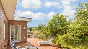 A patio with two lounge chairs and a table, a brick wall, and a glass door leading to an interior space. - House half 11 Dune 11 (ID 420) (Sankt Peter-Ording)