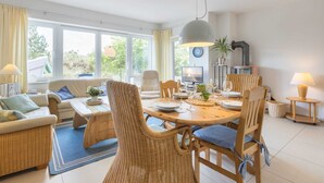 A dining area with wicker furniture, a round table, and a large pendant light. - House half 11 Dune 11 (ID 420) (Sankt Peter-Ording)