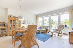 Un salon spacieux comprenant un coin repas, un ensemble de canapés, un fauteuil en osier et un téléviseur.