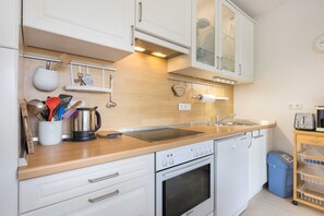 Une cuisine moderne avec des armoires blanches, un four en acier inoxydable, un lave-vaisselle et un plan de travail en bois.