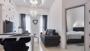 Un salon moderne avec un canapé, un téléviseur, un lustre et un décor en forme de cœur accroché au mur.