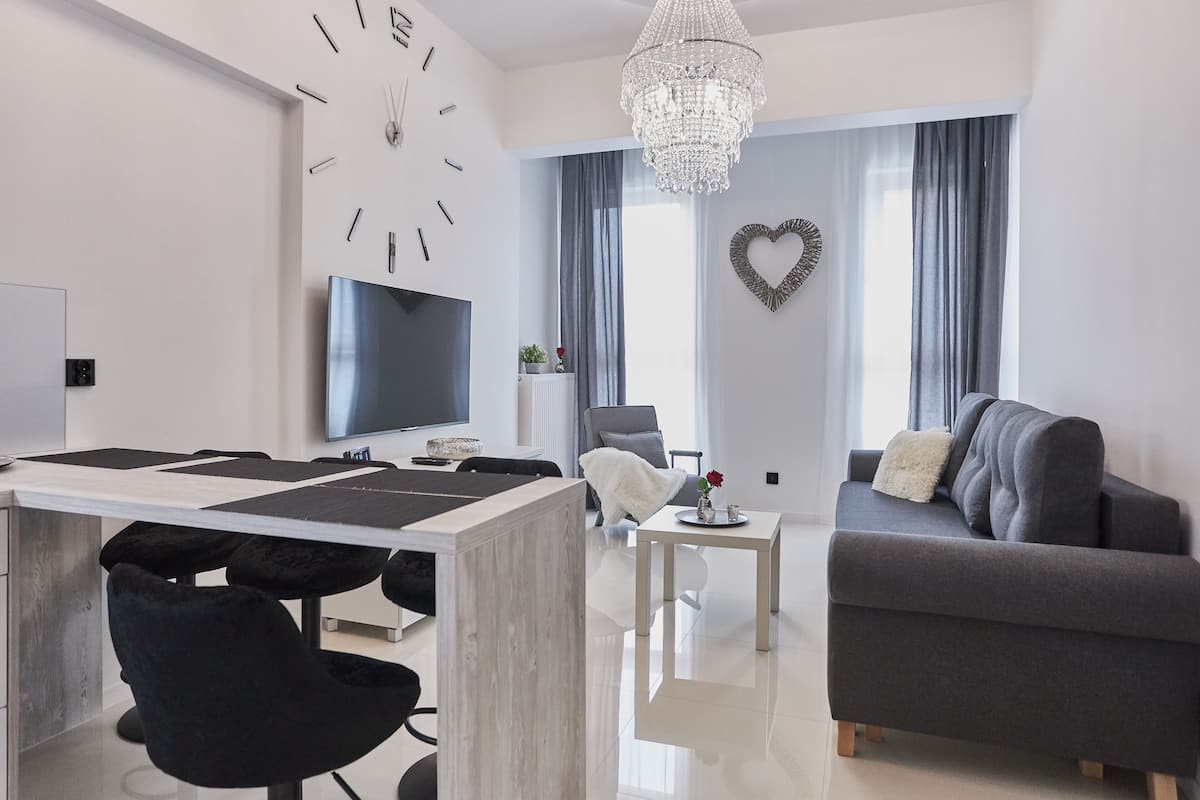 Uma sala de estar moderna com área de jantar, um candelabro, um relógio de parede grande e uma decoração em formato de coração.