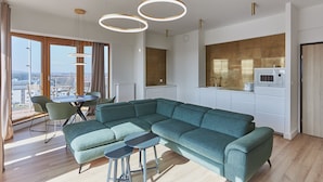 Un salon moderne avec un canapé d’angle, un coin repas avec une table et des chaises, et une cuisine équipée d’un four à micro-ondes.