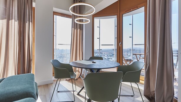 Un espace repas moderne avec une table ronde et quatre chaises, de grandes fenêtres avec des rideaux et une vue sur la ville.