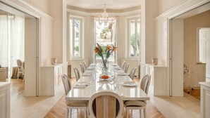 Un comedor espacioso con una larga mesa dispuesta para una comida, flanqueada por sillas y una lámpara de araña colgante.