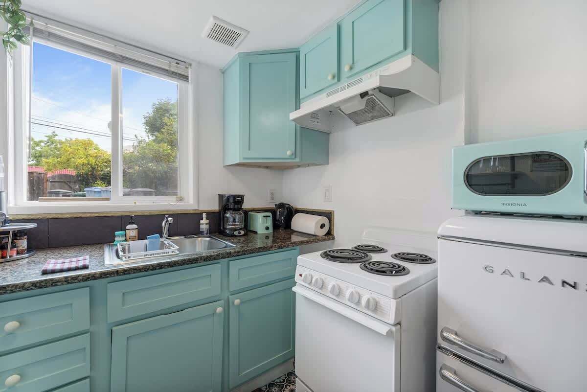 Cozinha com armários verde-água, fogão branco e janela com vista para o exterior.