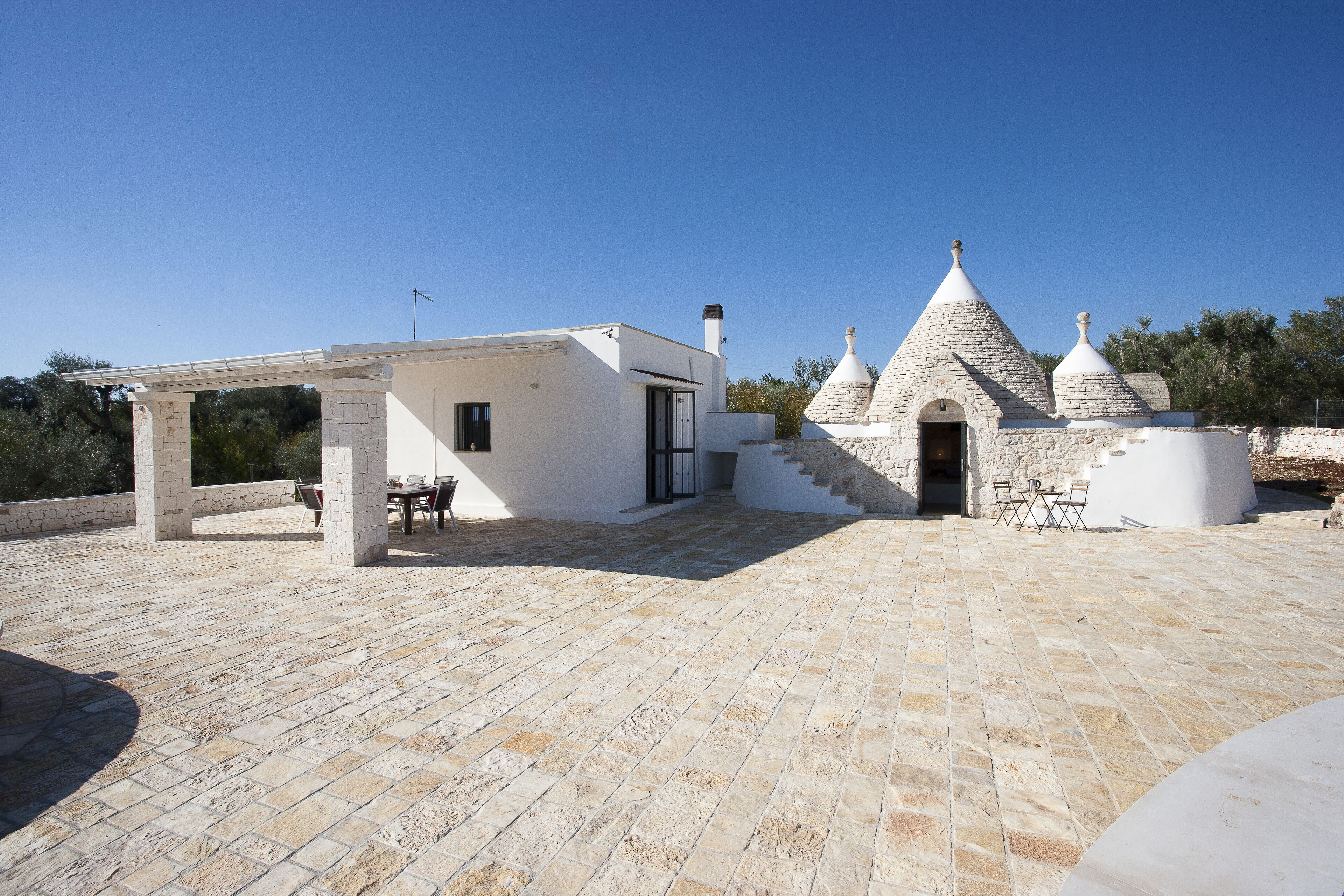 A rooftop terrace with stone flooring, a covered seating area, and a building with conical roofs.