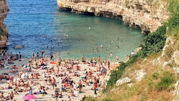 A coastal town with a rocky cliff and a beach populated with people. - ROMANTIC OR FAMILY RENTAL (Ceglie Messapica)