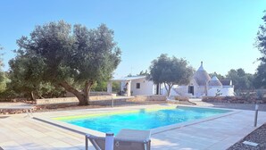 A swimming pool with a stone border, surrounded by pebbles and a few trees. - ROMANTIC OR FAMILY RENTAL (Ceglie Messapica)