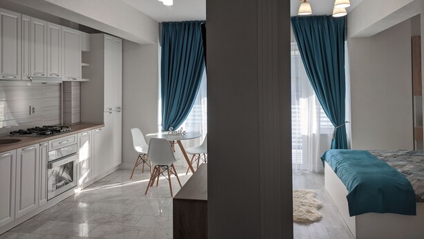 A modern kitchen with white cabinets, a dining area with a round table and chairs, and a bedroom with a bed and curtains. - Premium Apartment in Copou (Iași)