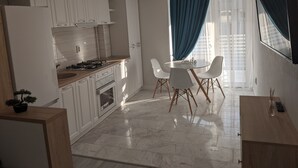 A modern kitchen with white cabinets, a gas stove, and a dining area with a table and chairs. - Premium Apartment in Copou (Iași)