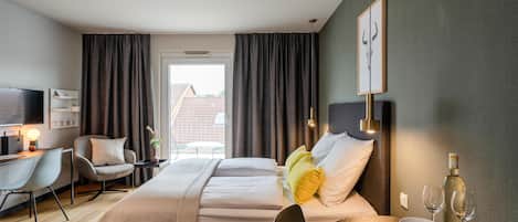 A hotel room with a bed, bedside table, chair, desk, and a view of the outside.