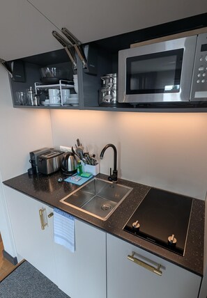 A compact kitchen with a microwave, toaster, sink, and stainless steel appliances. - ipartment Wolfsburg @HOME by Best Western (Wolfsburg)