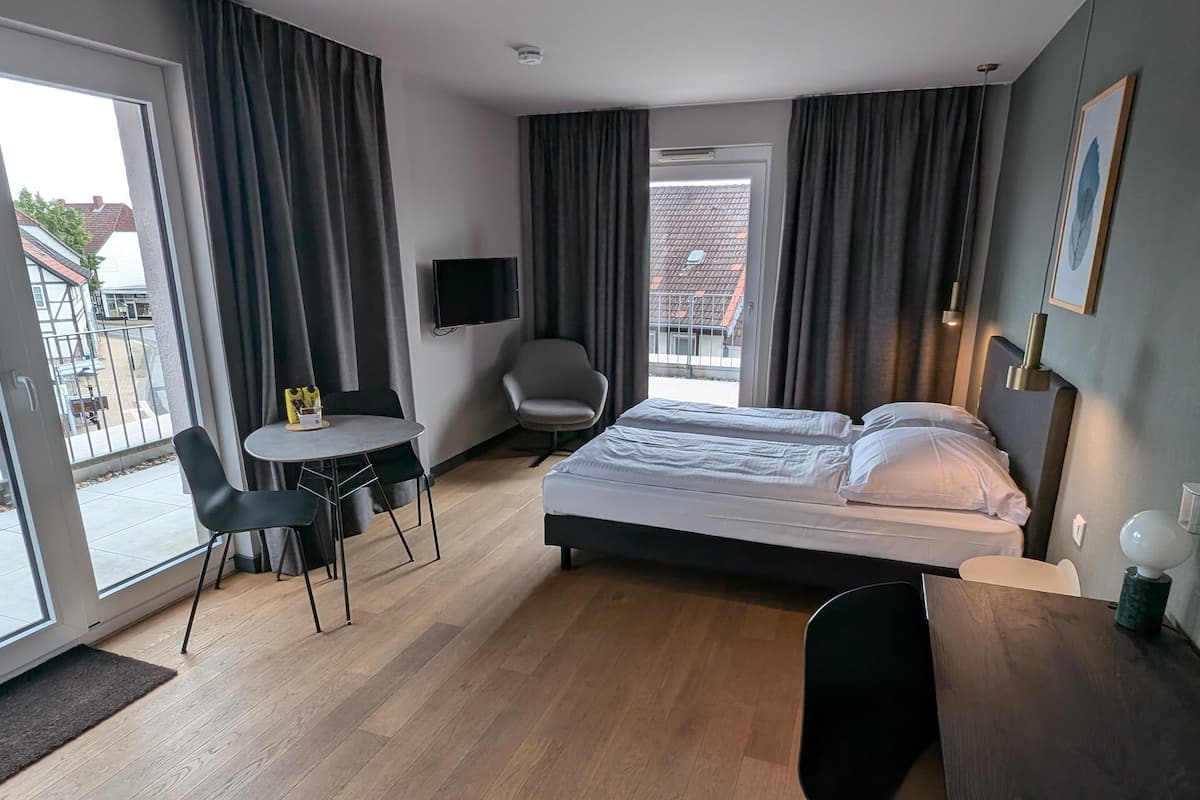 Une chambre d’hôtel avec un lit, un bureau, une chaise, une télévision et un balcon offrant une vue.