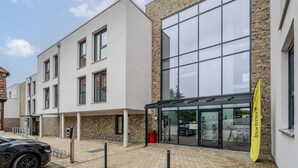A modern building with large windows, a covered entrance, and a yellow flag. - ipartment Wolfsburg @HOME by Best Western (Wolfsburg)