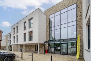 A modern building with large windows, a covered entrance, and a yellow flag. - ipartment Wolfsburg @HOME by Best Western (Wolfsburg)